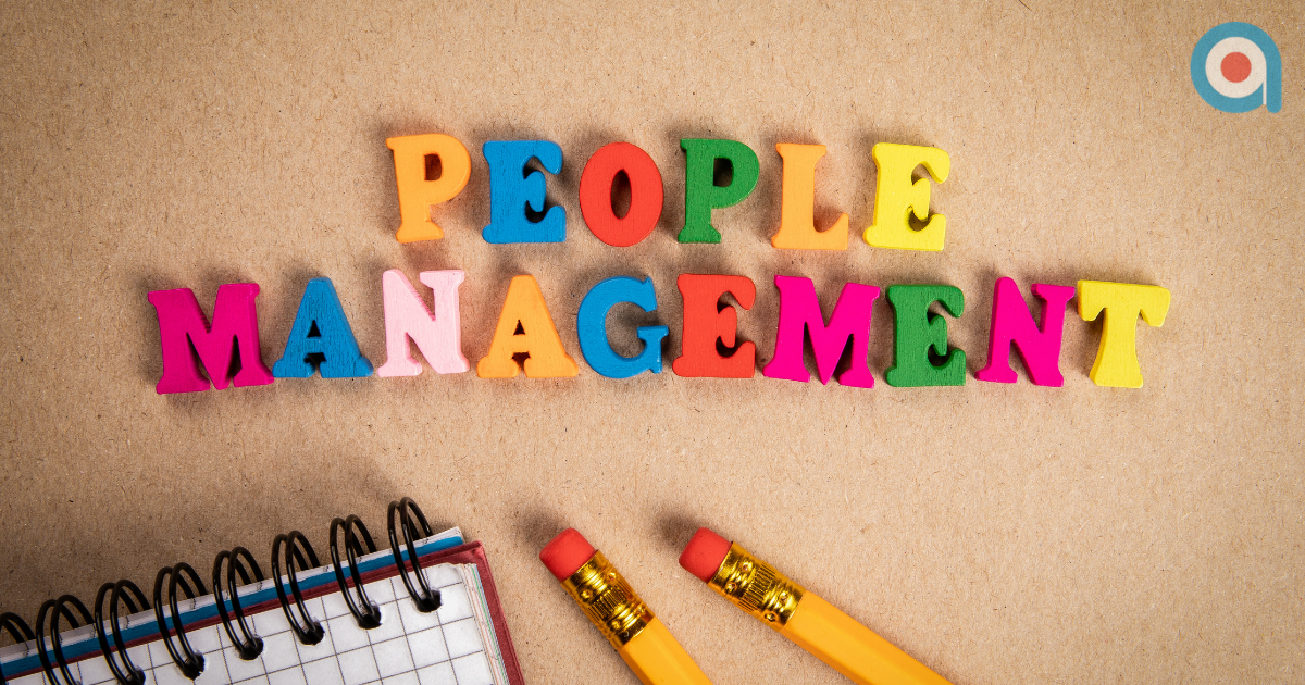 Toy letters spelling "PEOPLE MANAGEMENT" next to a notebook and pencils