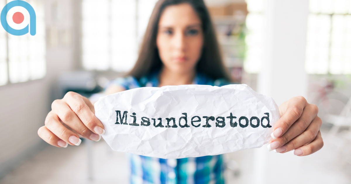 Woman in blue patterned top holding crumpled white paper with the word 'Misunderstood' printed in typewriter-style font, with Target Training Associates logo in top left corner